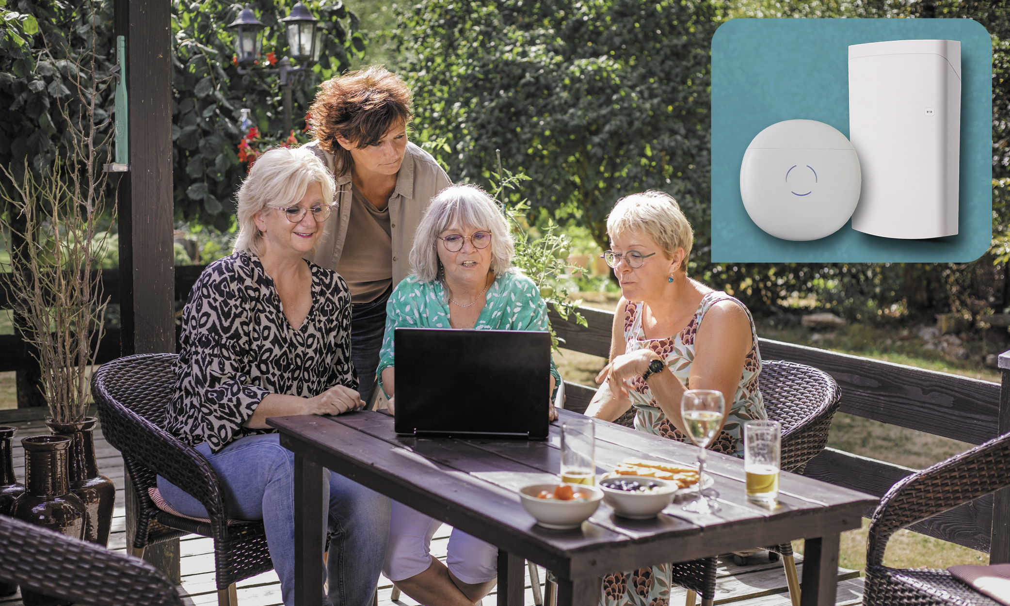 Four women gathered around an outdoor patio table looking at a laptop.